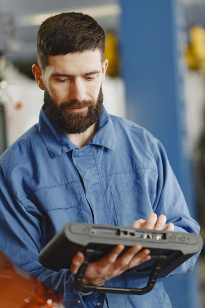 男人穿着工作服的汽车修理工拿着平板电脑在车旁边年轻人机械车库