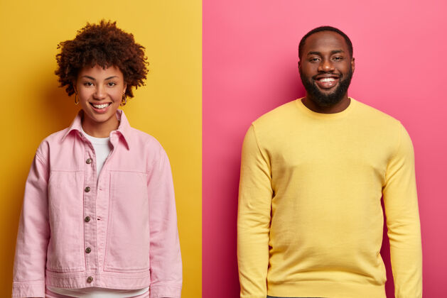 丈夫快乐的非洲裔美国人男女微笑着满意的水平镜头 靠着两面彩色的墙站在一起 很高兴听到对话者的好消息 一起工作胡须聚会快乐
