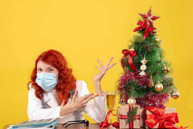 年份前视图女医生围绕圣诞树和礼物坐在面具病毒礼物肖像