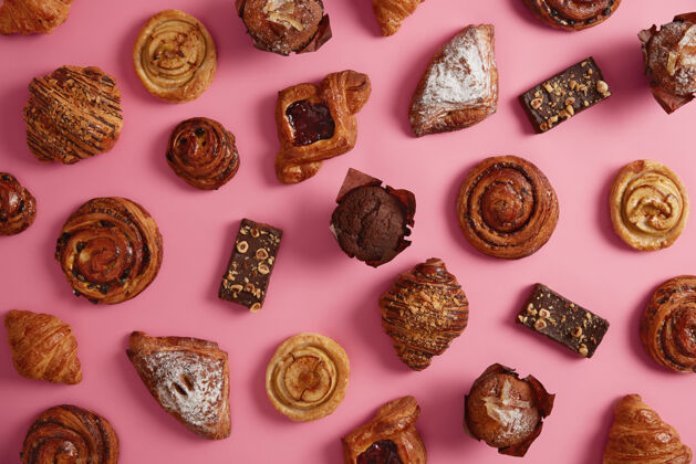 整个各种甜美开胃的烘焙产品 以玫瑰色为背景各种牛角面包 糖粉面包 果酱饼干 巧克力松饼 美味的面包卷各种糖果牛角包蛋糕顶部