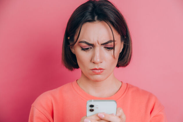 网站年轻女子在阅读手机短信时感到悲伤 不开心 愤怒 背景是粉色的成人信息心烦