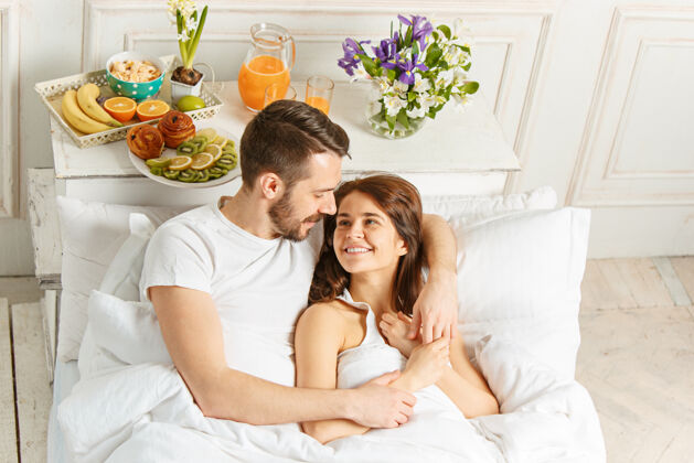 女性年轻的异性恋夫妇躺在卧室的床上醒来男性清醒