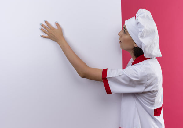 厨师穿着厨师制服的年轻白人厨师女孩惊讶地看了看 把手放在白色的墙上 粉色的上面留有复印空间空间手烹饪