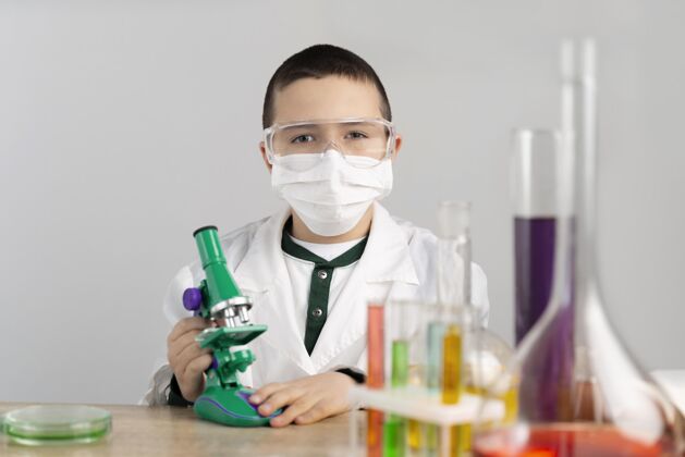 实验室外套实验室里拿显微镜的男孩科学科学防护眼镜