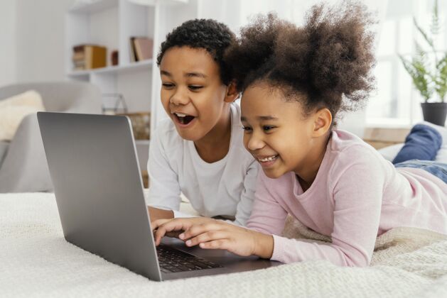 水平两个兄弟姐妹一起在家玩笔记本电脑的侧视图房子内部乐趣