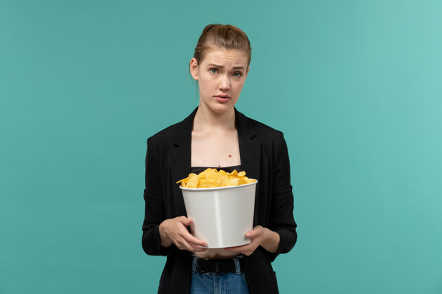 电影正面图：年轻女性在蓝色的水面上吃薯片看电影观看土豆咖啡