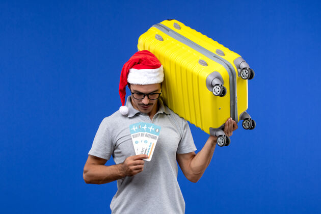 人正面图：年轻的男性拿着沉重的包和机票在蓝墙航班度假飞机上工人持有圣诞节