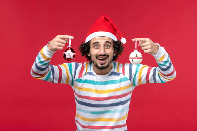 人正面图：年轻男子手持圣诞树玩具站在红墙上新年放假快乐成人前面