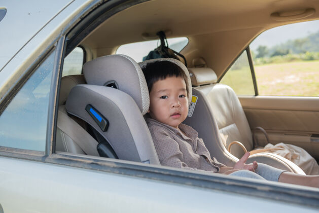 活动坐在儿童安全座椅上的小男孩耐心地坐在汽车后座上放松自由安全带