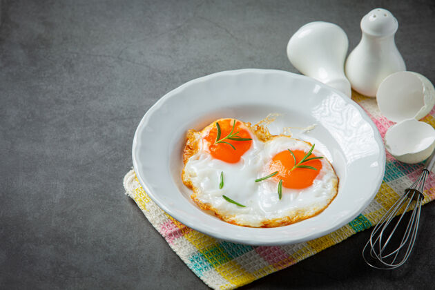 鸡蛋在黑暗的表面上用白色盘子煎鸡蛋蛋黄营养早餐