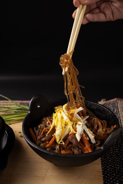 午餐一个人拿着木筷在灯光下煮好的玻璃面的垂直镜头营养面条中国菜