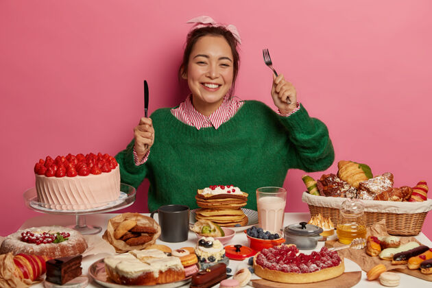 蜂蜜高兴的女人拿着叉子和刀 对甜点有着很好的胃口 有着牙齿般的微笑 享受着美味的菜肴 隔着粉红色的墙垃圾糖烹饪