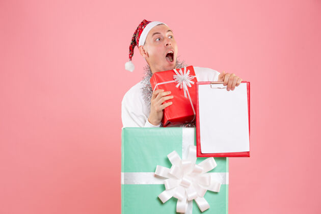 圣诞正面图年轻的男性在目前持有文件 目前在粉红色的背景粉色礼物视图
