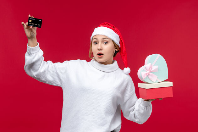 欢乐正面图年轻女子拿着礼物和银行卡在红地板上节日圣诞红礼物银行举行