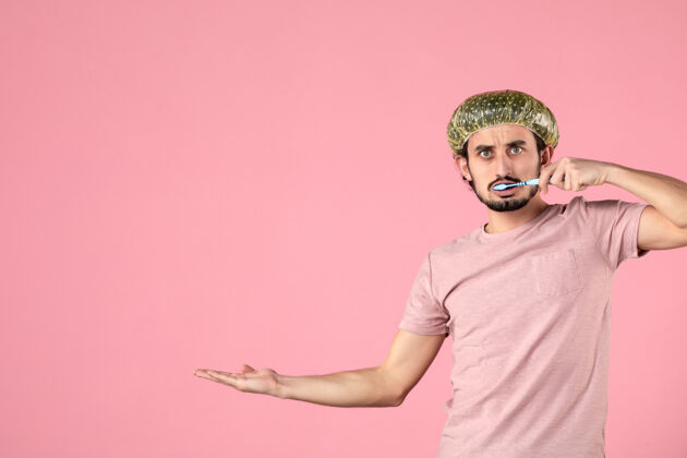 自我护理正面图：年轻男性在粉色背景上刷牙牙齿面部肖像
