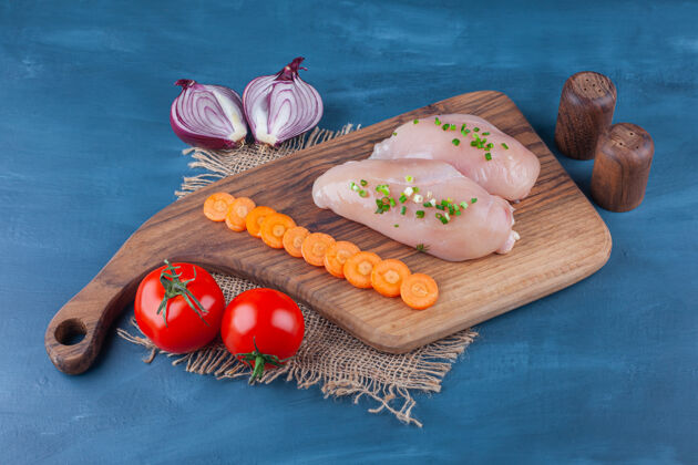 鸡肉鸡胸肉胡萝卜片放在砧板上 旁边是洋葱片 放在蓝色的桌子上美味有机食品