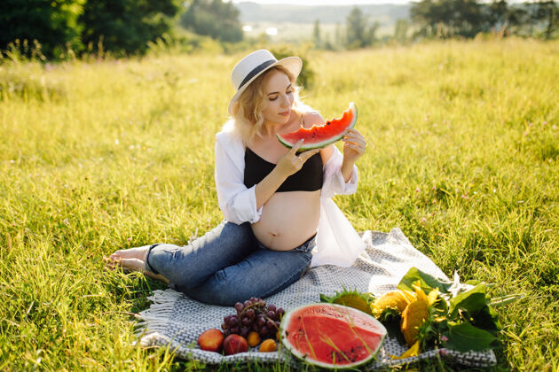 快乐年轻孕妇在公园户外放松 吃西瓜 健康怀孕坐着阳光肖像