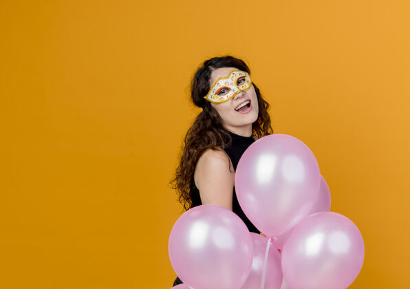 女人年轻漂亮的女人卷发手持一束气球在派对面具快乐快乐的生日派对概念超过橙色快乐站立束