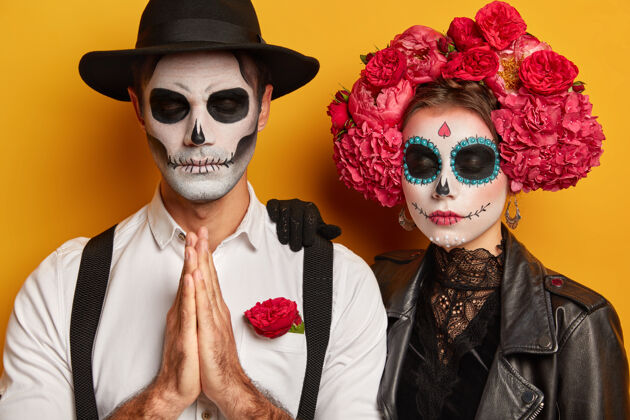 恐怖室内拍摄的可怕的夫妇头骨化妆 穿着传统的墨西哥服装 参观死亡嘉年华日 有鬼脸 男子站在祈祷姿势鬼魂化妆背带