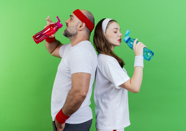 男人一对戴着头带和腕带的成年运动情侣背靠背地站在瓶子里喝水饮用水成人女人