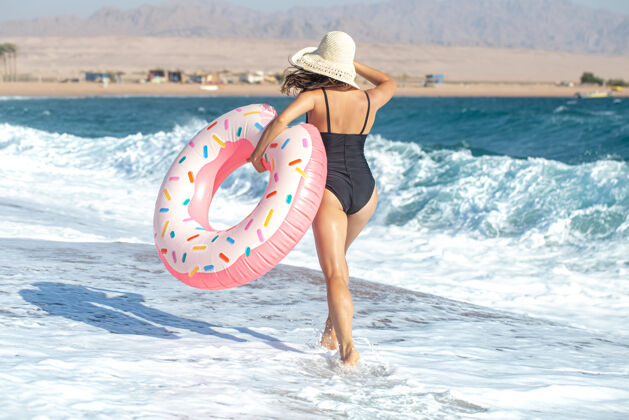 女人一个戴着帽子的女人 戴着一个甜甜圈 在海边游泳度假休闲娱乐的概念帽子黑发年轻