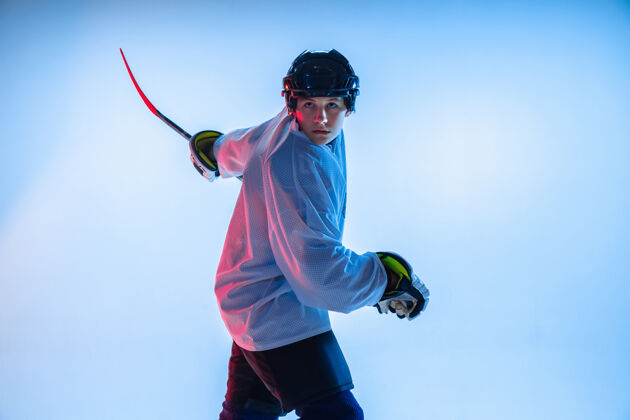 男孩年轻人年轻的男性冰球运动员 在霓虹灯下用棍子粘在白墙上运动员戴着设备和头盔练习运动的概念 健康的生活方式 运动 运动 动作运动员健康棒