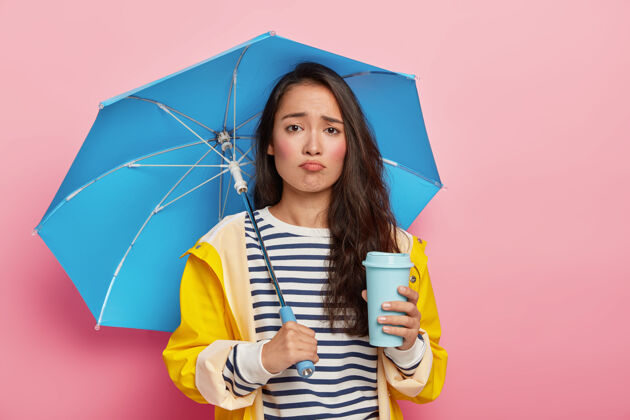 民族韩国人模样的垂头丧气的女人画像 因为天气不好而感到悲伤 天气预报不对 带着蓝色雨伞 穿着雨衣亚洲人秋天雨衣