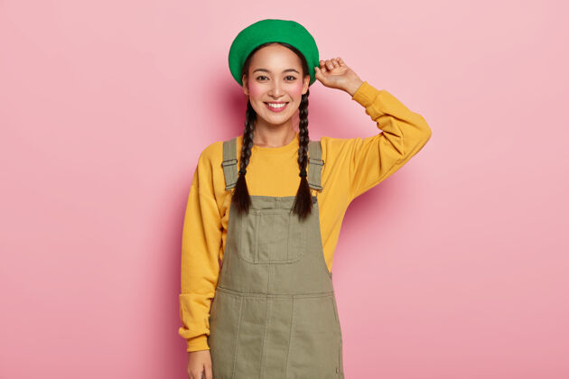 毛衣快乐的亚洲女模特有着胭脂的脸颊 有着愉快的面部表情 穿着时尚的贝雷帽 黄色的运动衫和牛仔裤年轻快乐请