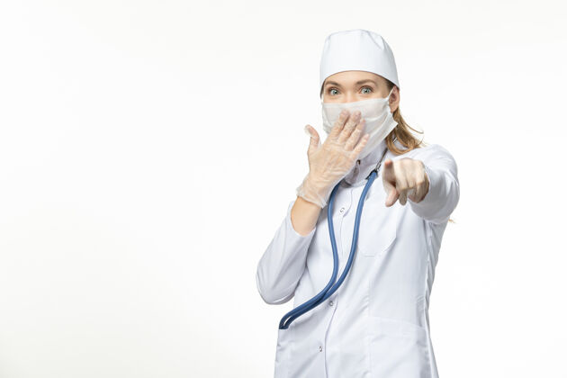 人正面图：穿着白色医疗服和面罩的女医生 在浅白的墙壁上保护自己免受冠状病毒的感染微笑防护正面