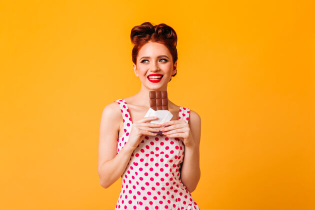 化妆品一个很幽默的欧洲女孩在吃巧克力一个穿着圆点裙的年轻女人在黄色的空间里微笑甜点复制空间连衣裙