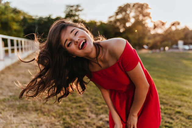 优雅一幅身着红色连衣裙的幽默少女的户外肖像 表达着幸福的心情一张棕色头发的快乐女孩在大自然中挥舞的照片幸福服饰时尚