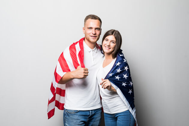 团结一对笑容可掬的夫妇手里拿着美国国旗 把自己隔离在白色的地面上青少年人微笑