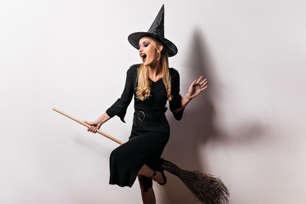 魔术师万圣节快乐的女巫骑着扫帚飞来飞去穿着黑色衣服的热情女巫的室内画像哥特式嘉年华服装