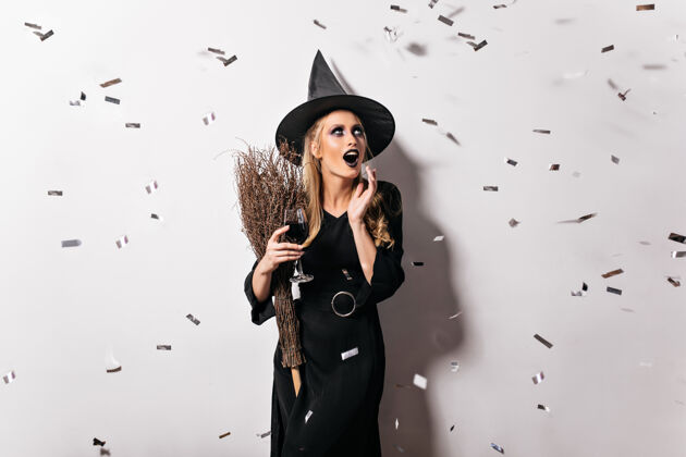 魔术戴着黑帽子的情绪化女巫在喝血高兴的女巫师拿着装有药剂的高脚杯肖像女巫金发