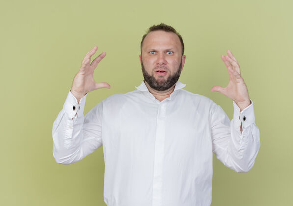 看一个留着胡子的男人穿着白衬衫 站在光墙上 展示着大尺寸的手势测量符号大小立场胡须