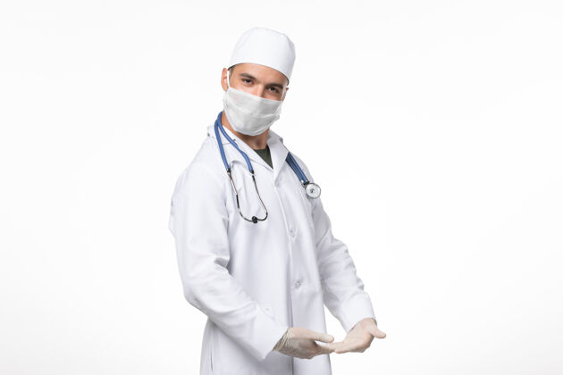 医生正面图：男医生穿着医疗服 戴着口罩 在白色墙壁上摆着柯维德病毒大流行病毒病的姿势视图冠状病毒冠状病毒防护