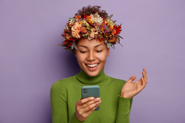 旁边漂亮的笑脸女人用手机 正扬起手掌咯咯地笑 戴着象征性的秋天花环和绿色套头衫离开站立秋天