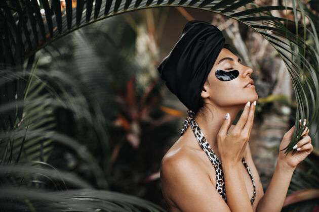 无忧无虑可爱的女人戴着黑色头巾站在自然的背景上在棕榈树附近的优雅女士的眼睛补丁户外拍摄异国情调女人热带