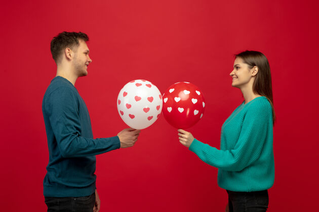 拥抱美丽的情侣爱上了红色工作室墙上的气球礼物盒子微笑