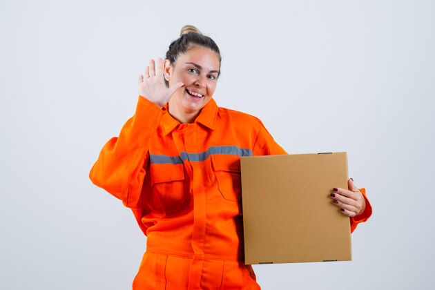女性年轻的女性在展示告别手势的同时 拿着一个工人制服的盒子 看起来很高兴前视图再见制服时尚