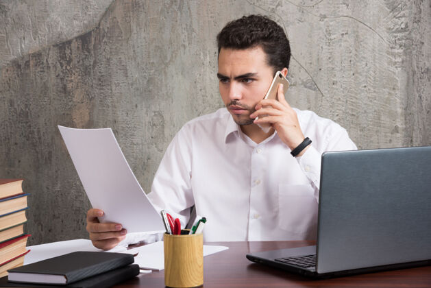 笔记本电脑办公室员工拿着一张纸在手机上聊天高质量的照片电话电话男