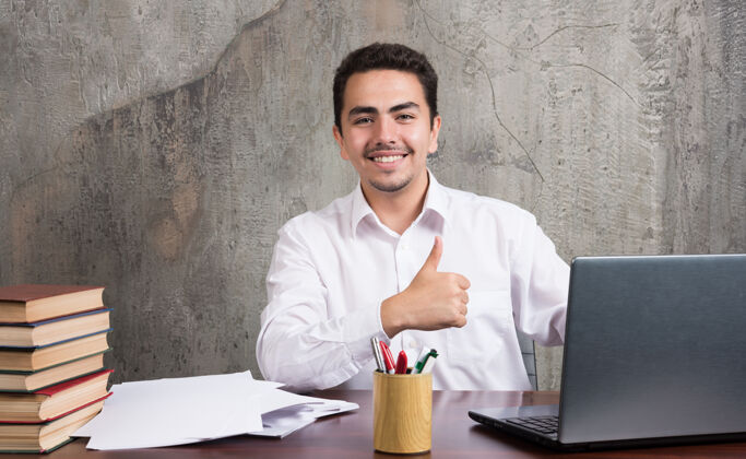 员工微笑的男人竖起大拇指坐在桌子旁高质量的照片笔记本电脑办公室男人