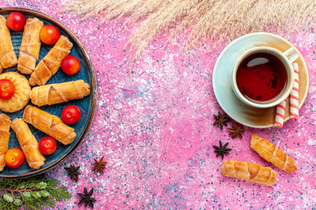美味的顶视图甜甜可口的百吉饼内托盘与新鲜的酸李子和一杯茶在淡粉色的桌子上托盘酸的咖啡