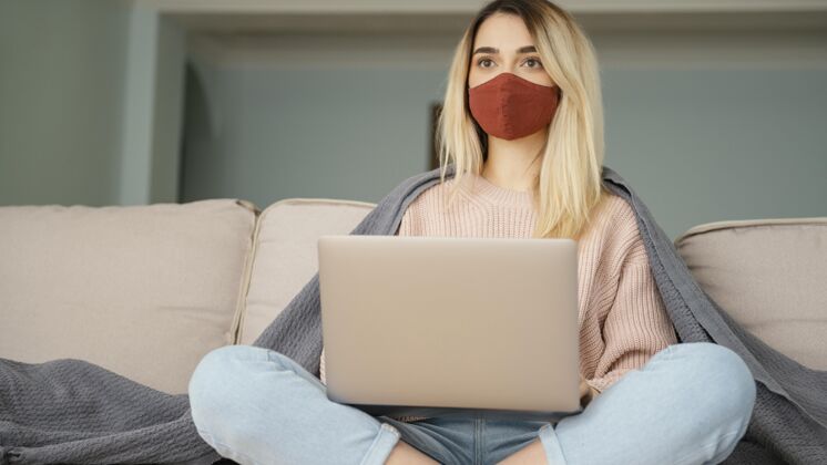 外科医生面罩呆在室内的女人戴着医用口罩拿着笔记本电脑室内大流行病毒