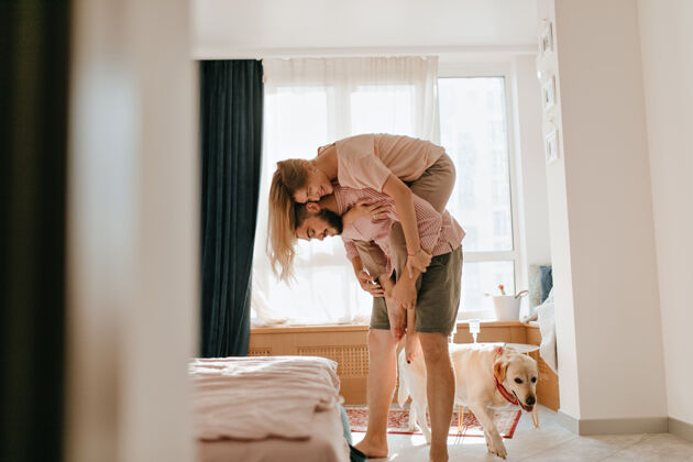 宠物穿着卡其色短裤的男人背着年轻的妻子 他们的狗在旁边散步情侣们在他们的公寓里享受无忧无虑的周末微笑情人房子