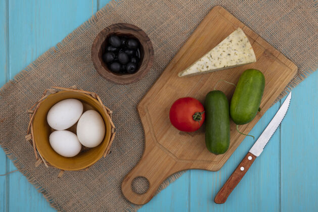 橄榄色顶视图切菜板上的黄瓜和西红柿芝士 米色餐巾上的鸡蛋和橄榄上衣切的乡村风味