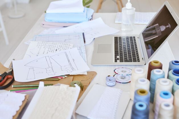 Couturier高角度的笔记本电脑与服装线计划和线轴在桌子上的工作室时尚商务Outfitter