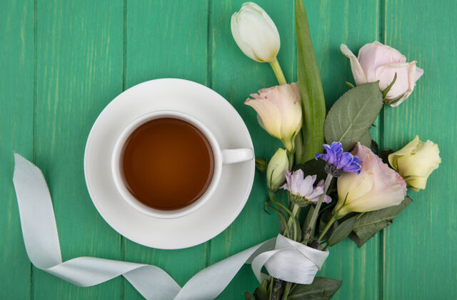 饮料一杯茶的顶视图 绿色木质背景上有雏菊玫瑰和郁金香之类的花茶杯子雏菊