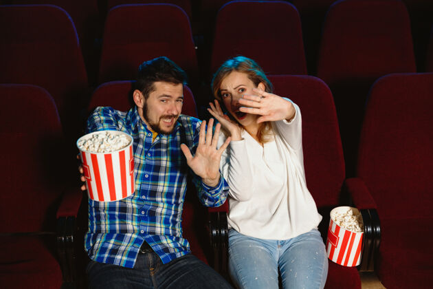 吃迷人的年轻白种人夫妇在电影院 房子或电影院看电影看起来富于表现力 惊讶和情绪化独自坐着玩关系 爱情 家庭 周末时间观众情侣表达