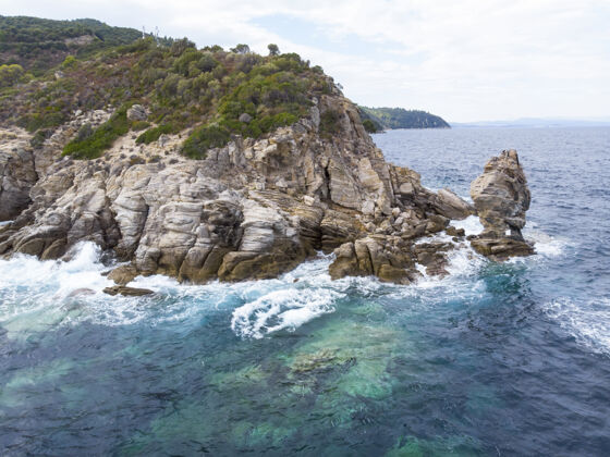 海岸爱琴海沿岸碧波荡漾 碧波荡漾 周围绿意盎然 岩石 灌木丛和树木 从无人机希腊俯瞰希腊海岸悬崖